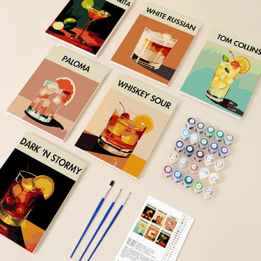 Classic Cocktails -numeromaalaussetti, jossa kuusi 20x15 cm drinkkiteemaista maalausta nimillä, maalipurkit, pensselit ja ohjeet pöydälle aseteltuna.